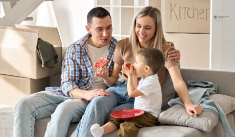 Happy Family New Tenants With Kid Sitting On Couch At New Home At Moving Day.