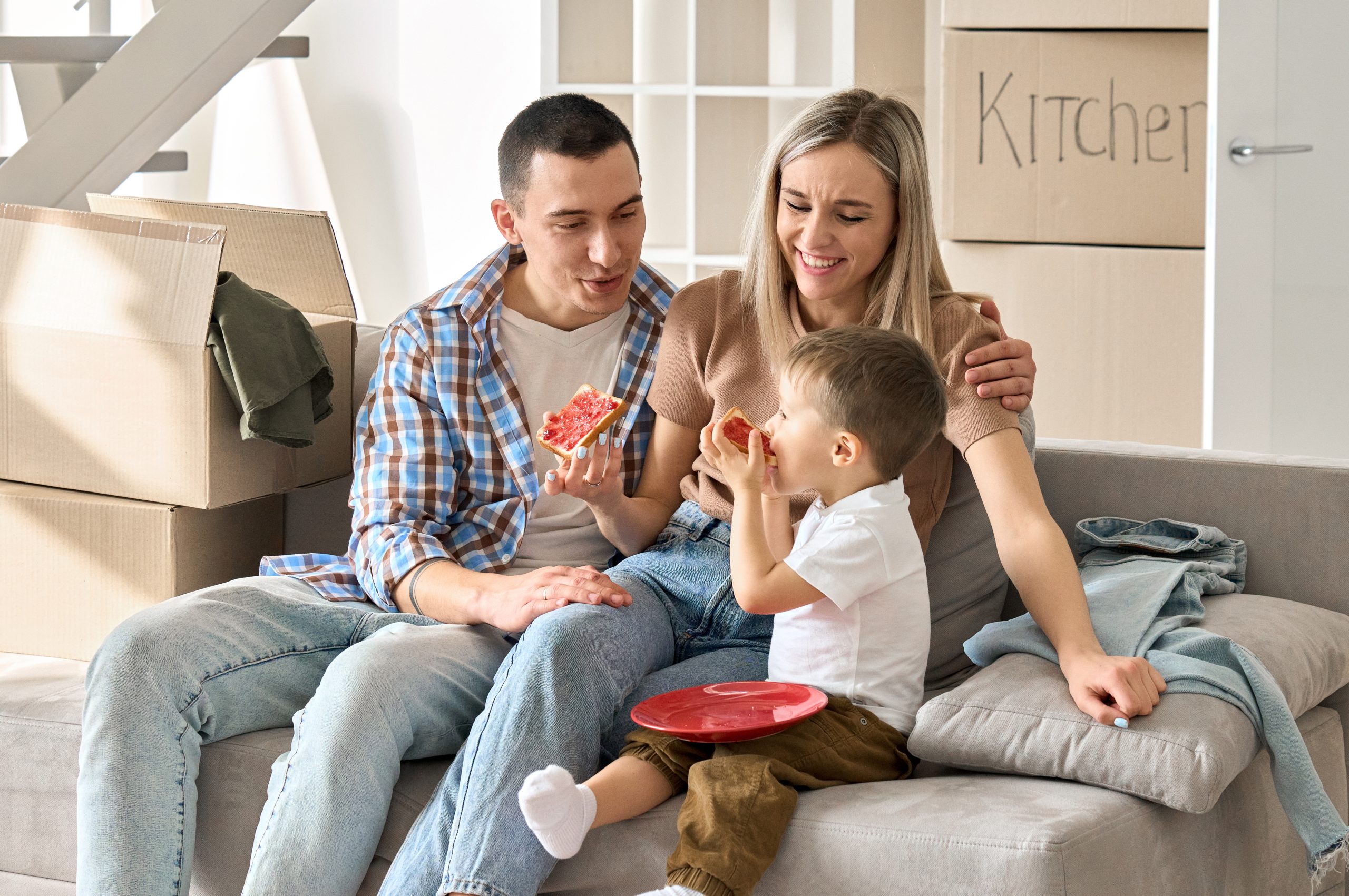 Happy Family New Tenants With Kid Sitting On Couch At New Home At Moving Day.